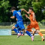 man in blue and orange jersey shirt running on green grass field during daytime